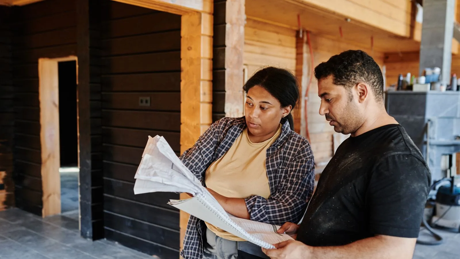 Two contractors in dusty workwear reviewing project drawings inside a building under construction