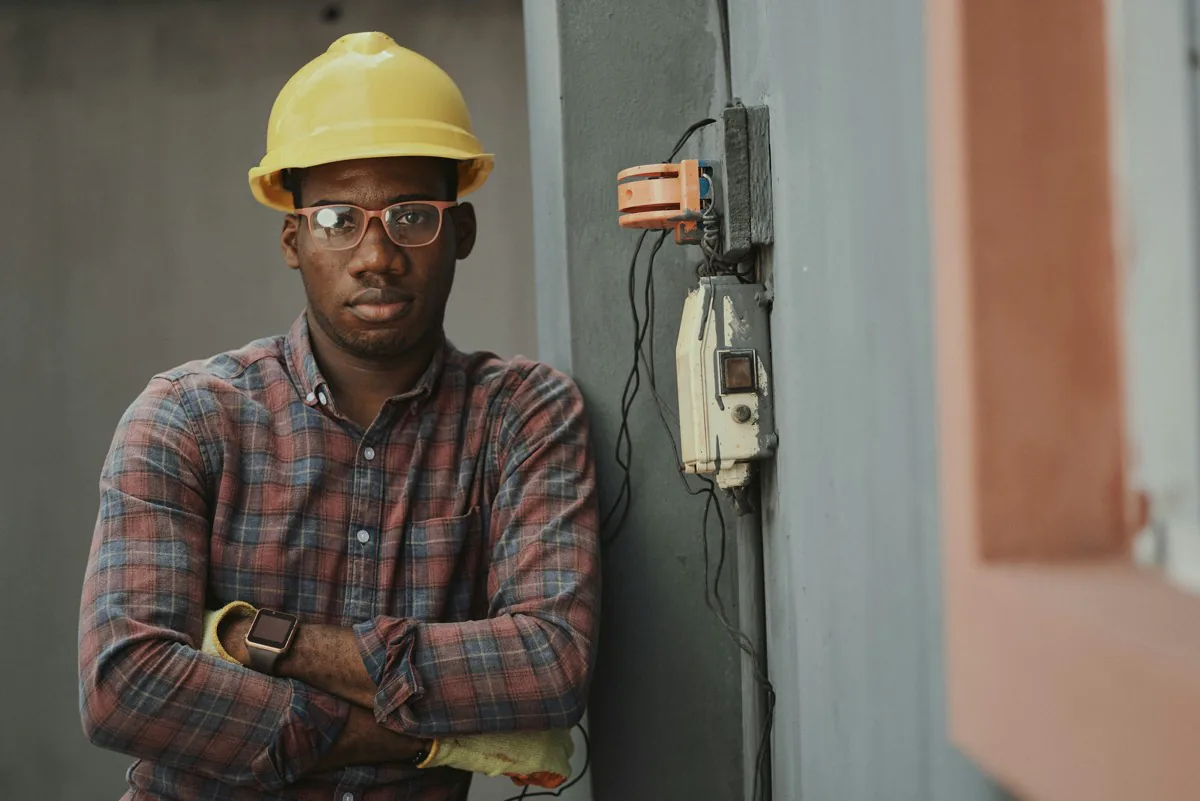 Editorial portrait of a contractor in a hard hat standing beside an electrical service box on a job site.