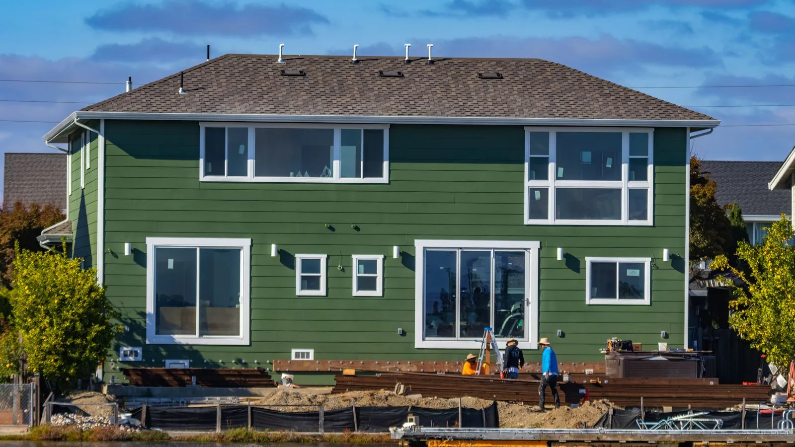 Crew working at the rear of a house with new green siding, new windows and a deck going in