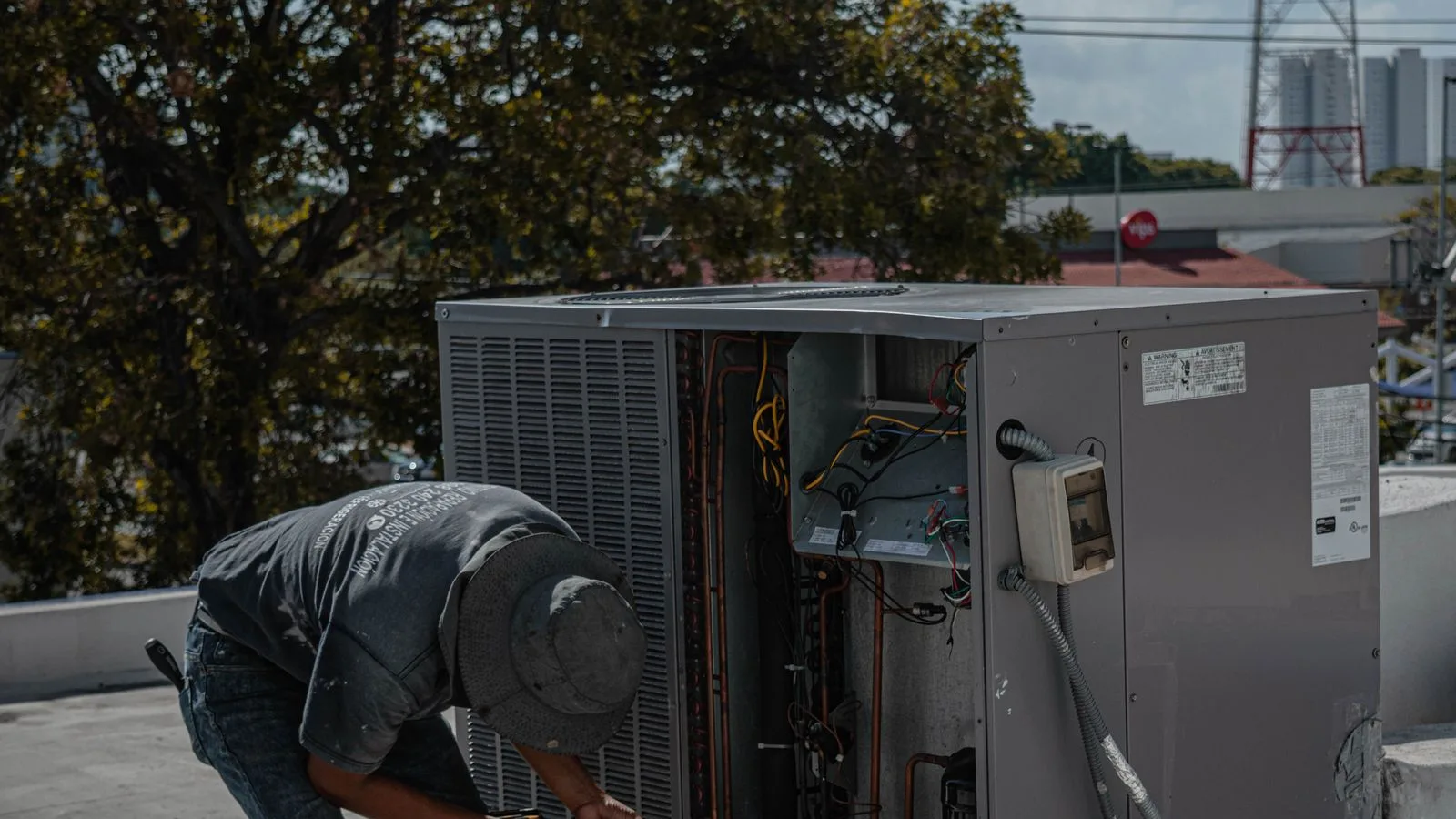 HVAC technician using a drill inside an opened rooftop condenser unit, coils and wiring exposed