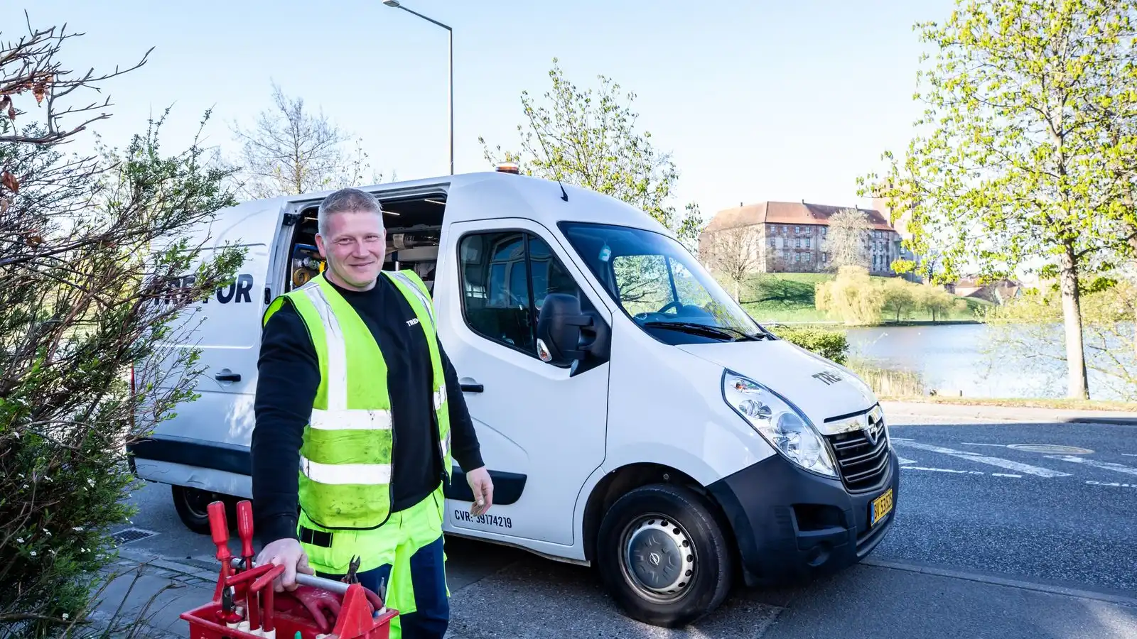 Home services technician in a hi-vis vest carrying a toolbox beside his branded service van