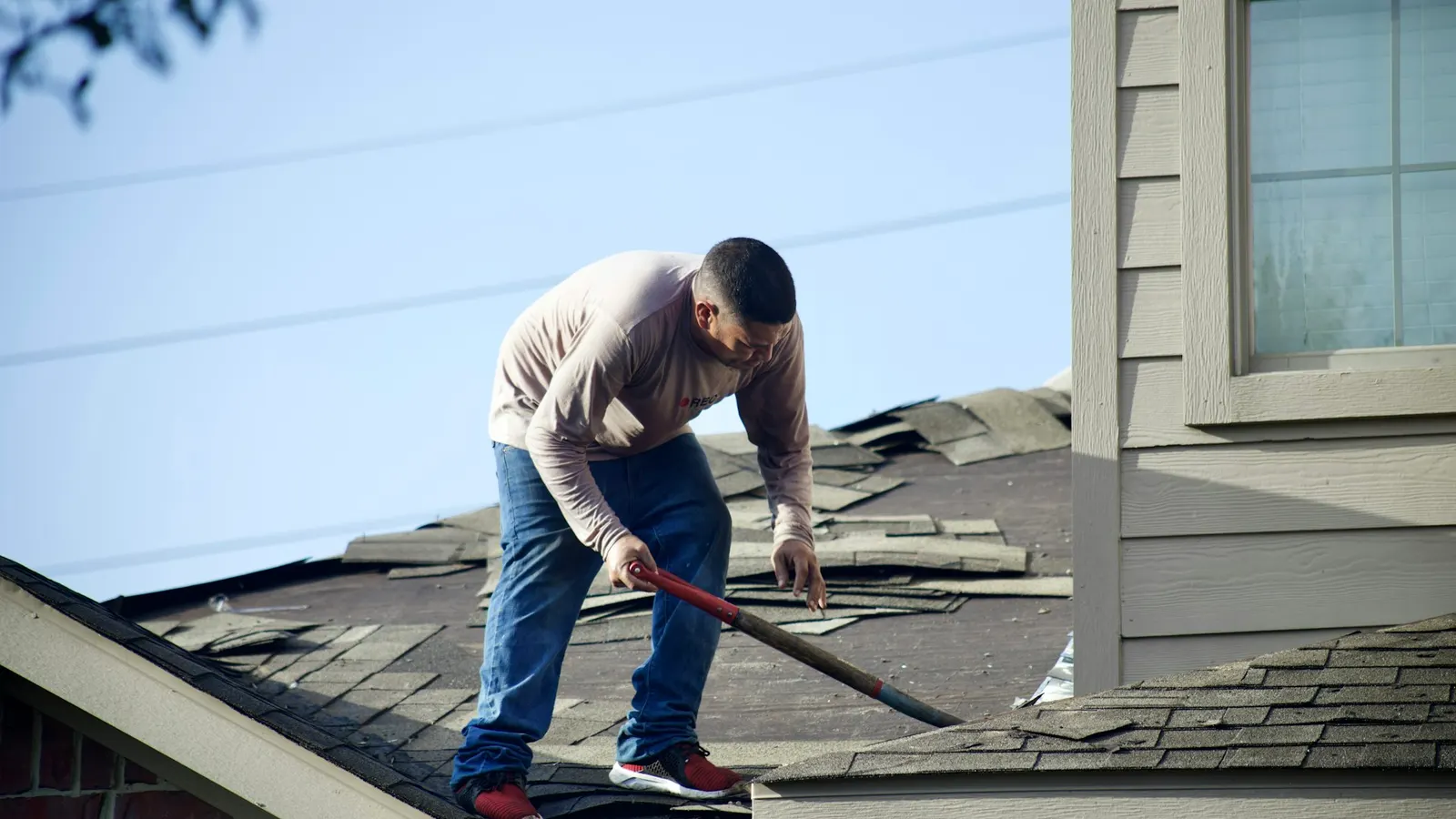 Roofer removing old shingles from a residential roof during a tear-off