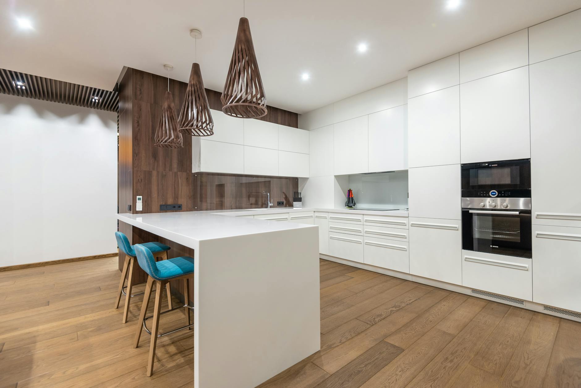 Chairs at table near white cupboards and modern kitchenware with oven in spacious stylish kitchen with hanging lamps in contemporary flat