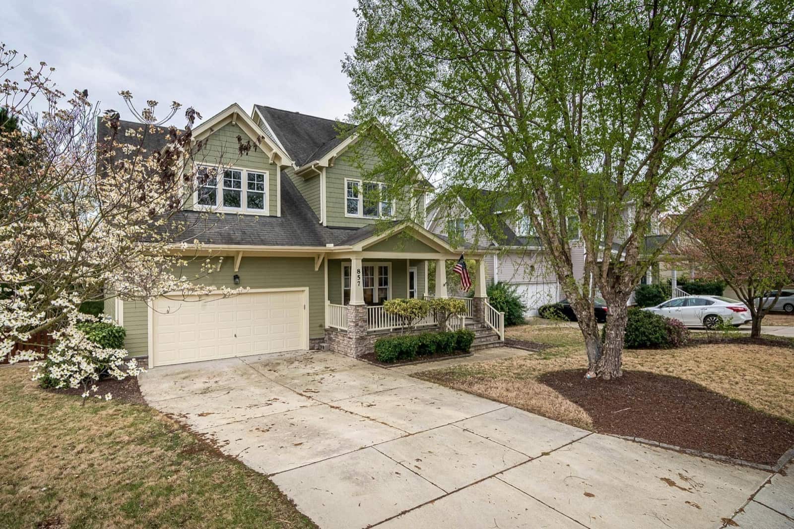 A picturesque suburban home with a lush front yard, driveway, and trees.