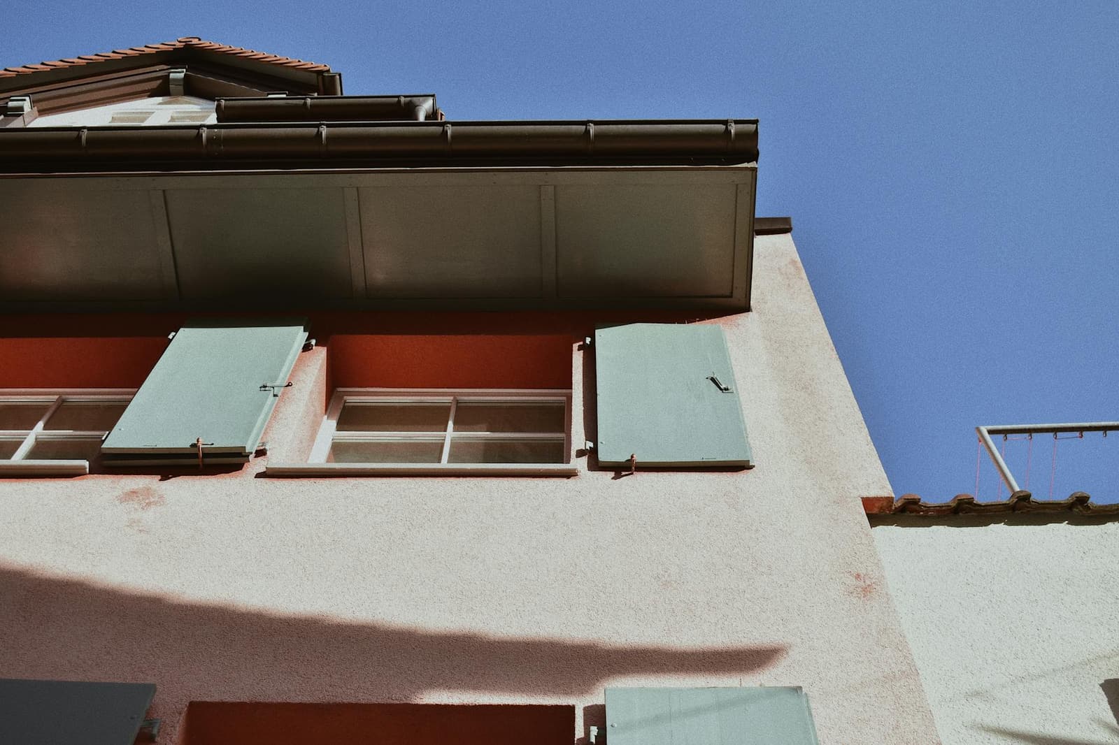A close view of a building exterior showcasing distinctive green shutters against a pastel facade.